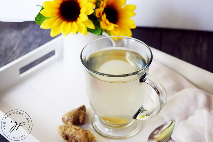 A glass mug filled with Fresh Ginger Tea, sitting on a white serving tray.