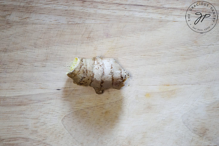 A knob of fresh ginger sits on a cutting board.