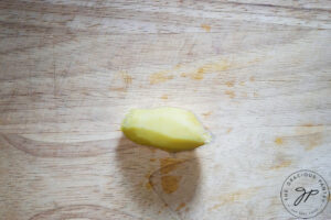 A peeled knob of fresh ginger sits on a cutting board.