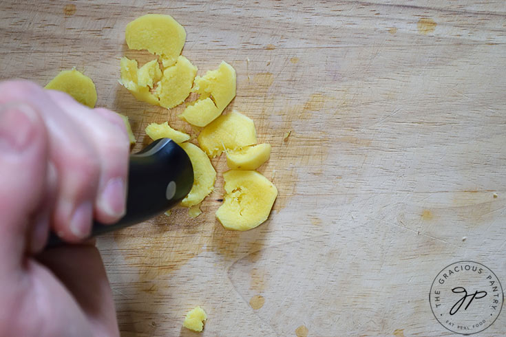 The handle of a knife crushing slices of fresh ginger.