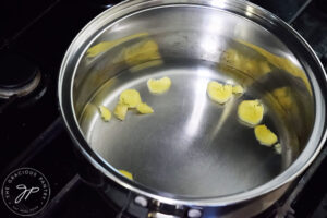 Water with fresh ginger slices in a pot, sitting on a stovetop.