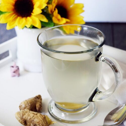 A mug of hot, Fresh Ginger Tea sits on a white serving tray next to some fresh ginger.