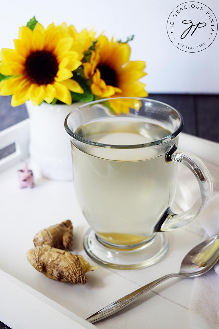 A mug of hot, Fresh Ginger Tea sits on a white serving tray next to some fresh ginger.