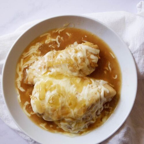 An overhead view looking down into a white bowl that holds two French Onion Chicken breasts.