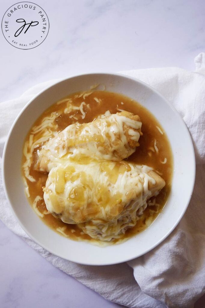 An overhead view looking down into a white bowl that holds two French Onion Chicken breasts.