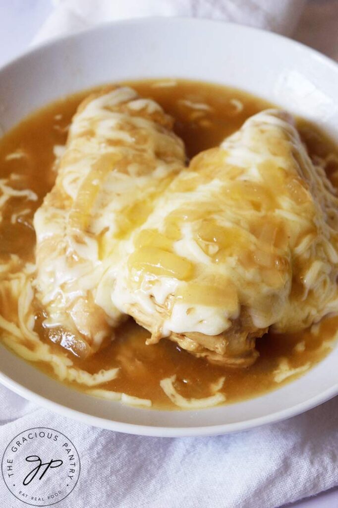 A side view of a white bowl holding French Onion Chicken breasts with mozzarella cheese melted over the top.