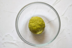 A ball of matcha energy ball dough sits in a glass mixing bowl.