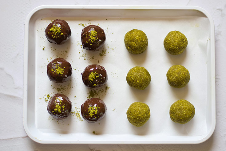 Matcha Energy Balls sit on a parchment lined cookie sheet. Half of them have been dipped in melted chocolate.