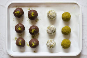Matcha Energy Balls on a parchment-lined baking pan. Some dipping in chocolate, some in grated coconut, and some plain.