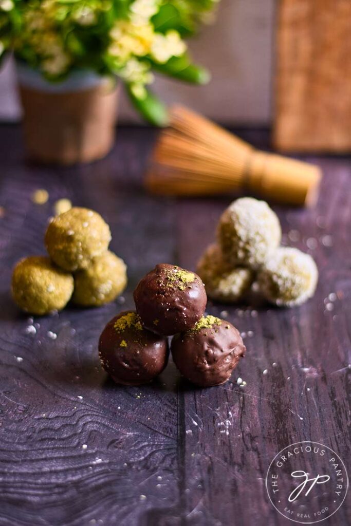 Three groups of three different types of matcha energy balls sit on a wooden surface.