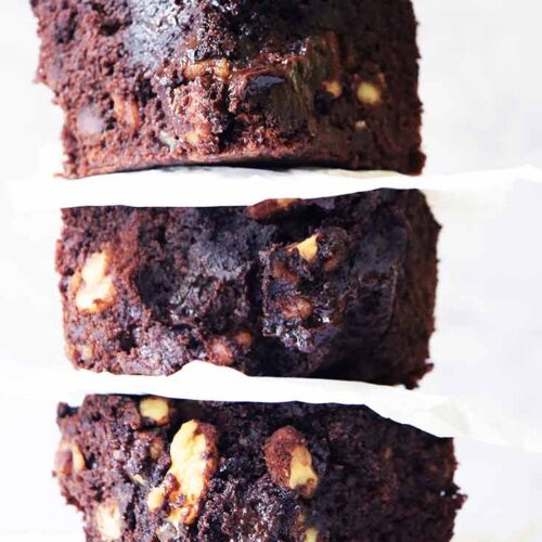 A close up shot of three oat flour brownies stacked up on a white background.