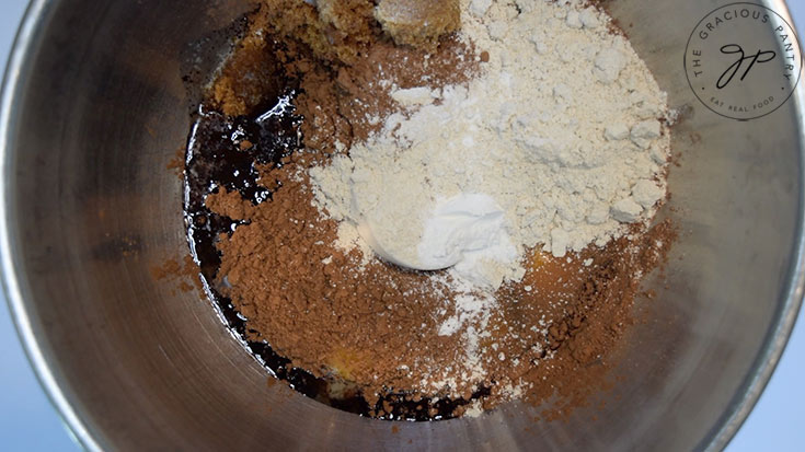Flour and cocoa powder added to other ingredients in a mixing bowl.