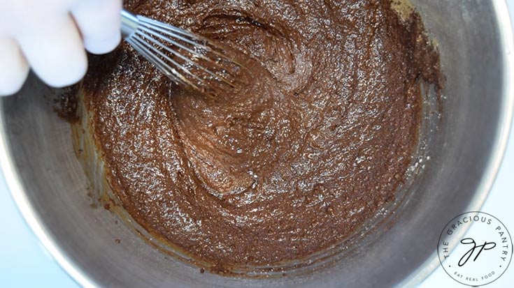 Mixing up brownie batter in a stainless steel mixing bowl with a whisk.