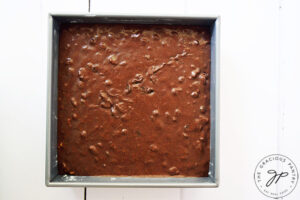 Brownie batter poured sitting in a square cake pan.