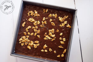 Walnuts sprinkled over the top of raw brownie batter in a square cake pan.