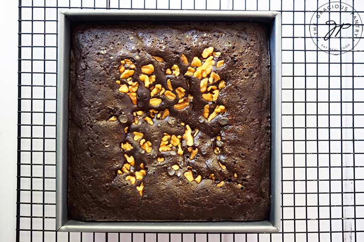 Just baked, oat flour brownies in a square cake pan, cooling on a black, wire, cooling rack.