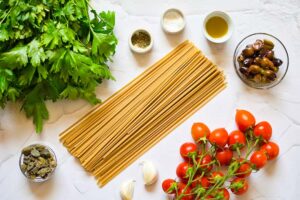 All the ingredients for this Easy Pasta Puttanesca Recipe gathered on a white surface.