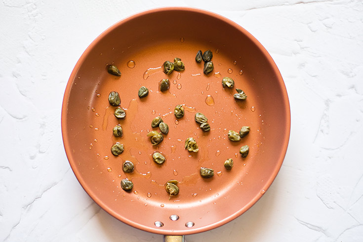 Capers sitting in olive oil in a skillet.