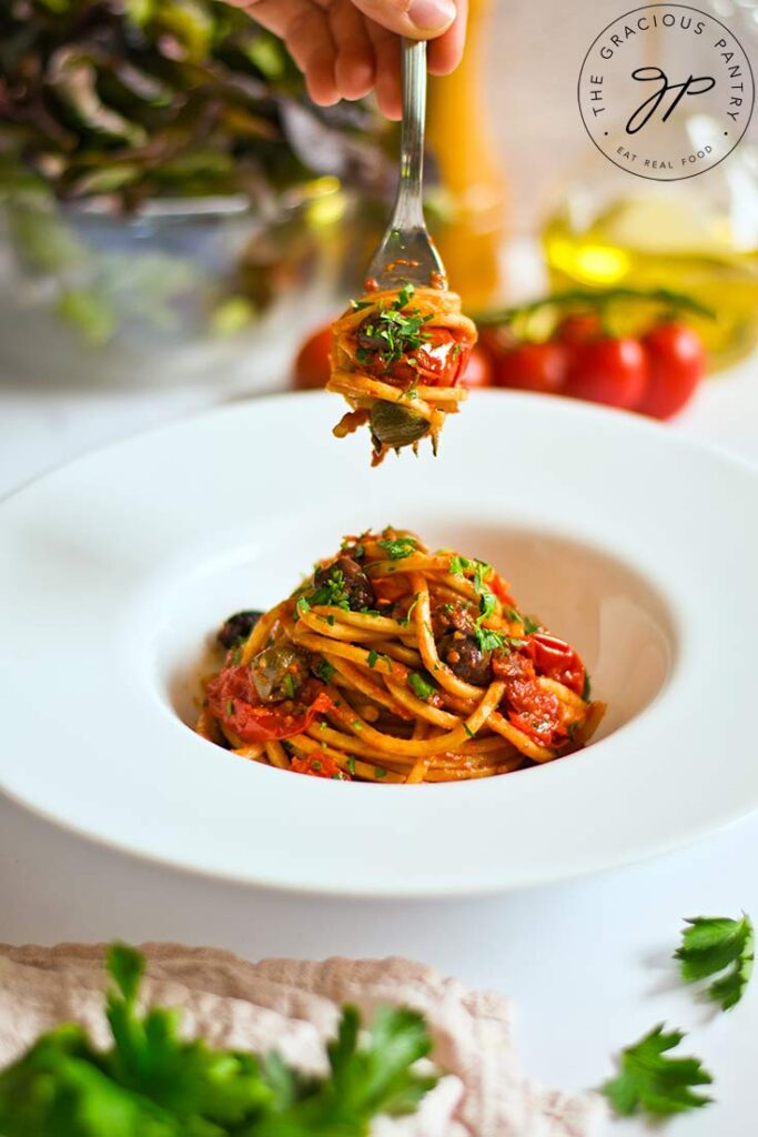 A fork lifts some of this Easy Pasta Puttanesca out of a white bowl.