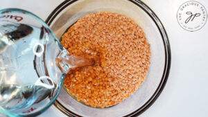 Boiling water being poured into a glass bowl filled with red lentils.