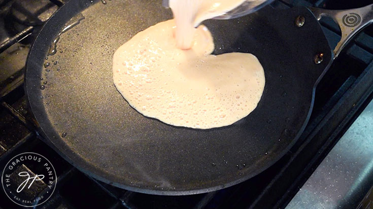 Red lentils wraps batter being poured onto a crepe pan.