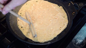 Red lentil wraps batter being spread over a crepe pan with a crepe spreader.