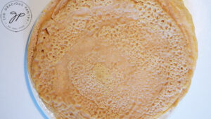 A white plate on a white background holds a stack of red lentil wraps.