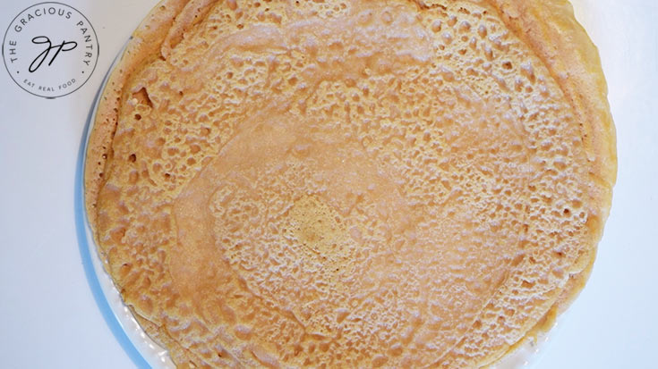 A white plate on a white background holds a stack of red lentil wraps.