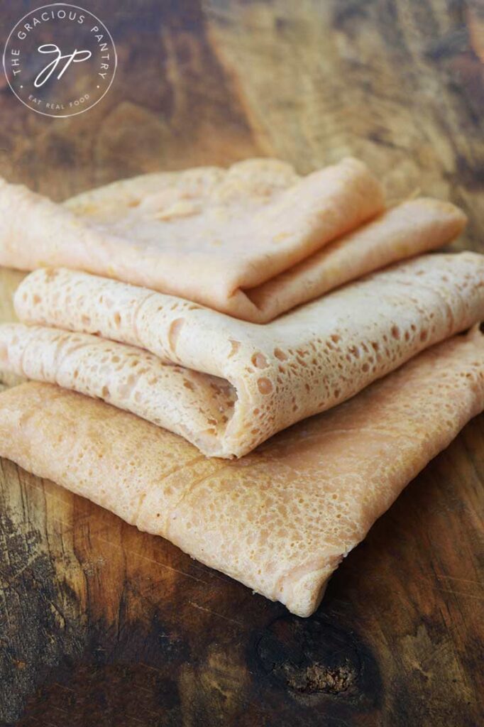 A front view of folded red lentil wraps sitting on a wooden cutting board.