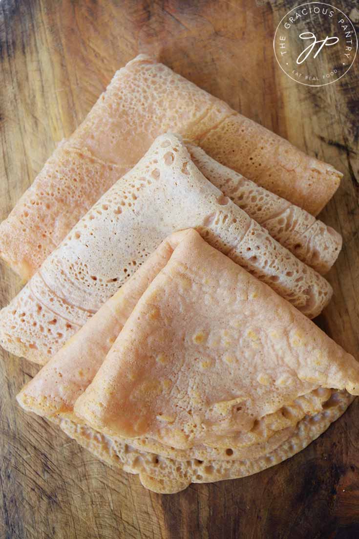 An overhead view of a stack of folded red lentil wraps laying on a wooden cutting board.