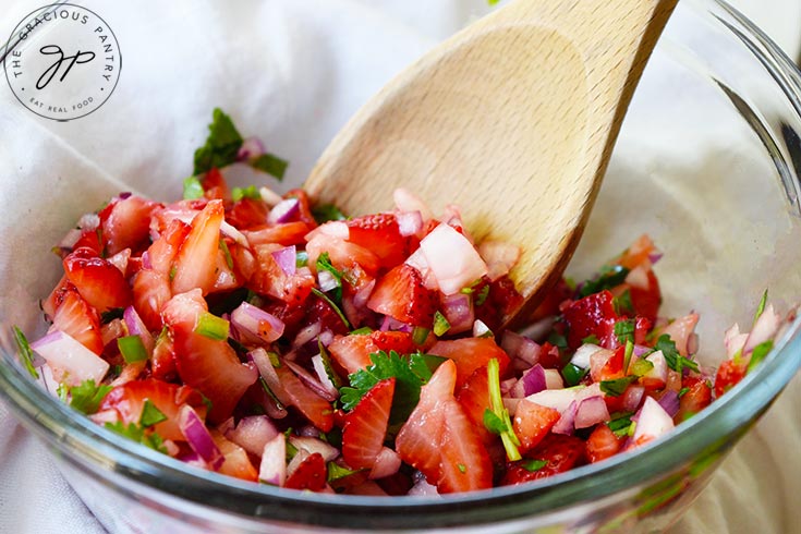 Finished Strawberry Salsa in a glass mixing bowl with a wooden spoon.