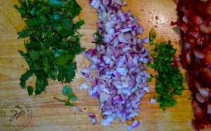 Chopped cilantro, onions, jalapeno peppers and strawberries sitting on a wooden cutting board.