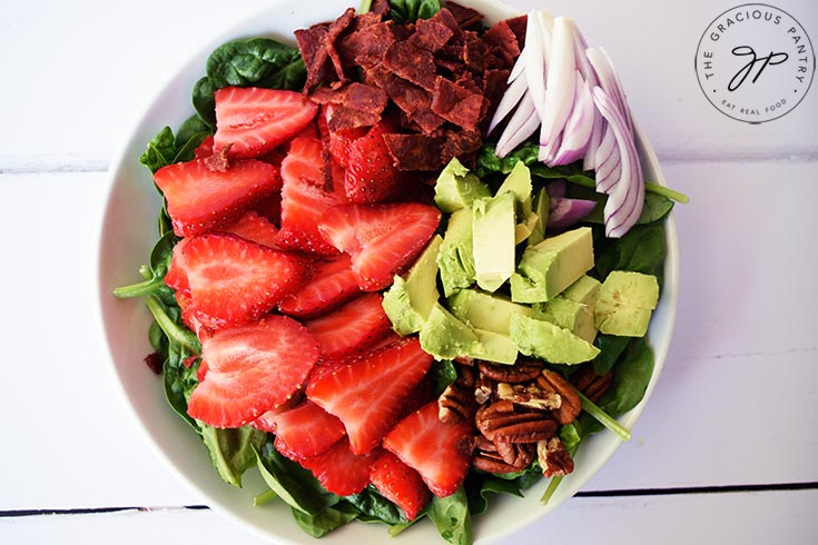 An overhead view looking down into a white bowl filled with Strawberry Spinach Salad.