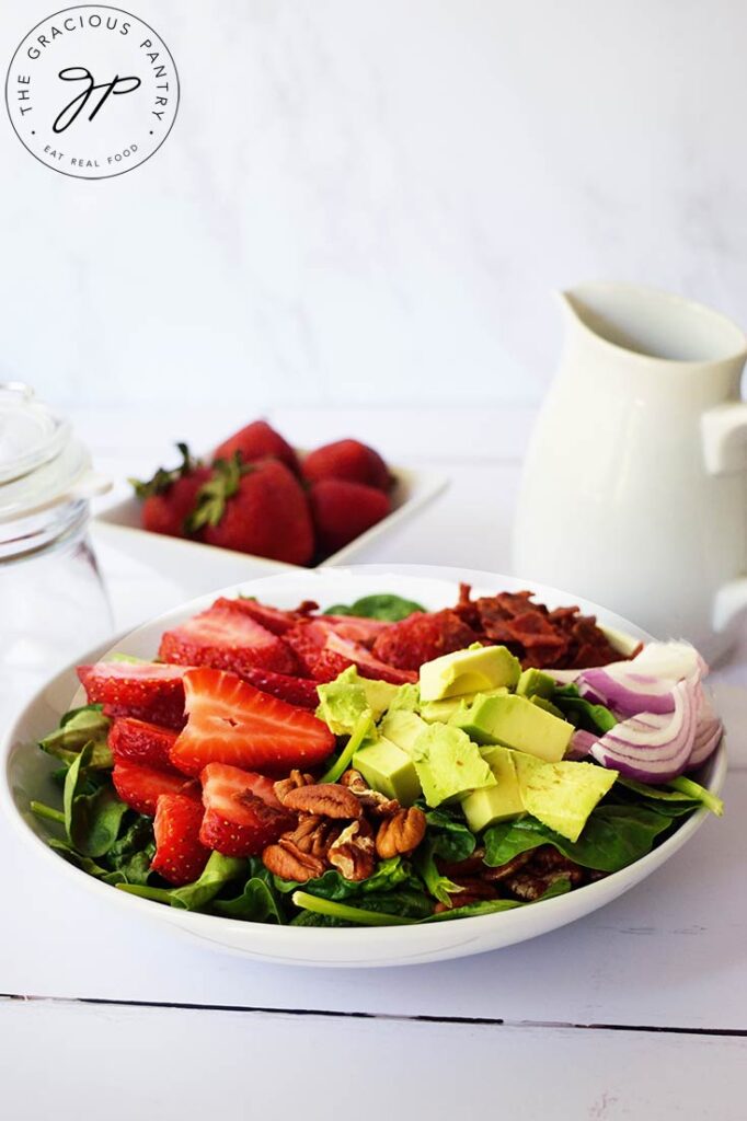 A side view of a white bowl filled with all the components of a Strawberry Spinach Salad.