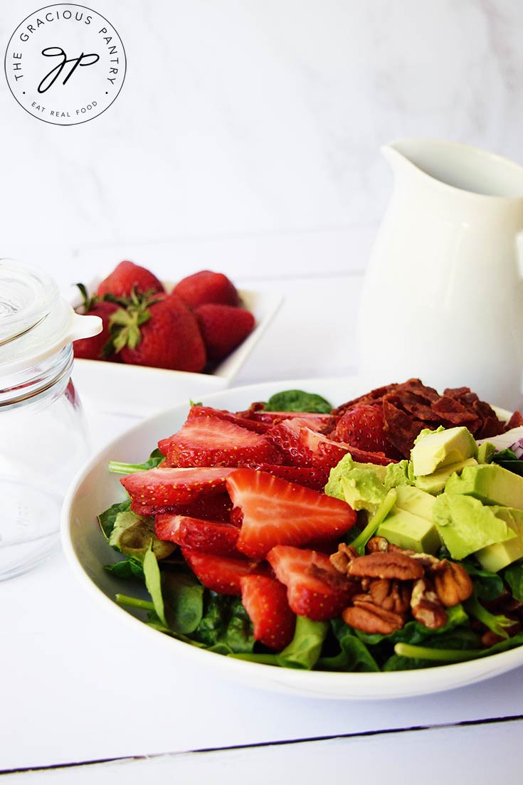 A white bowl sits on a white surface and is filled with Strawberry Spinach Salad.