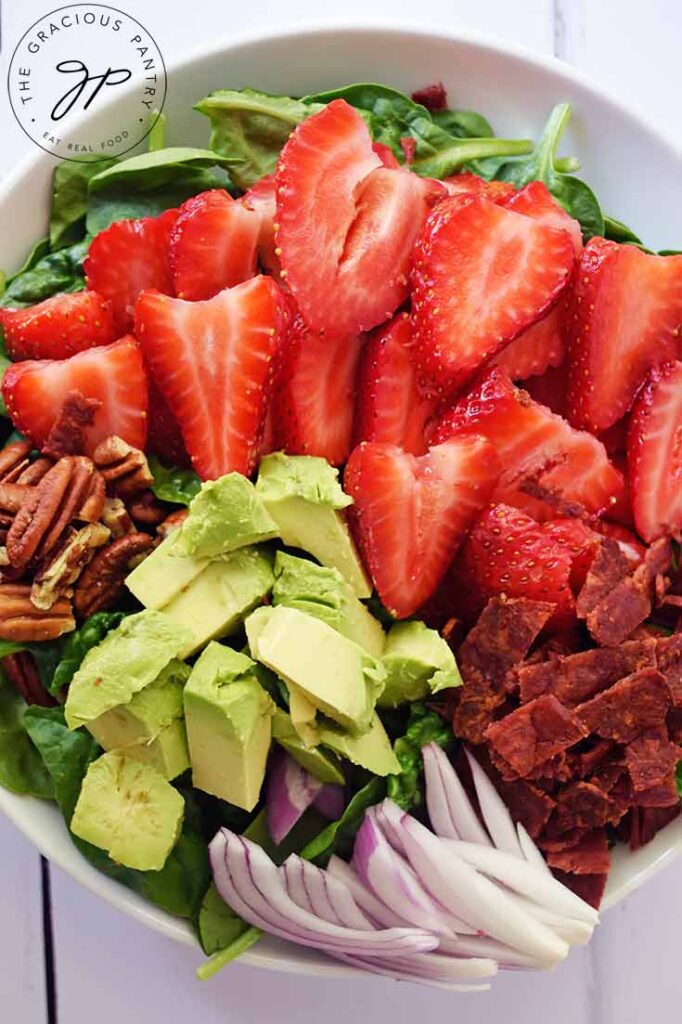 An overhead view of a white bowl filled with Strawberry Spinach Salad.