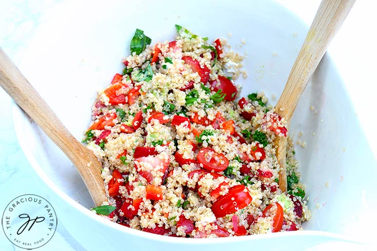 The finished Summer Quinoa Salad Recipe in a mixing bowl with two wooden spoons resting in the bowl.