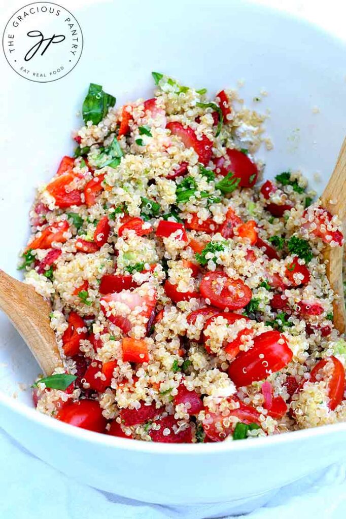 A close look at Summer Quinoa Salad sitting in a white mixing bowl with two wooden spoons.