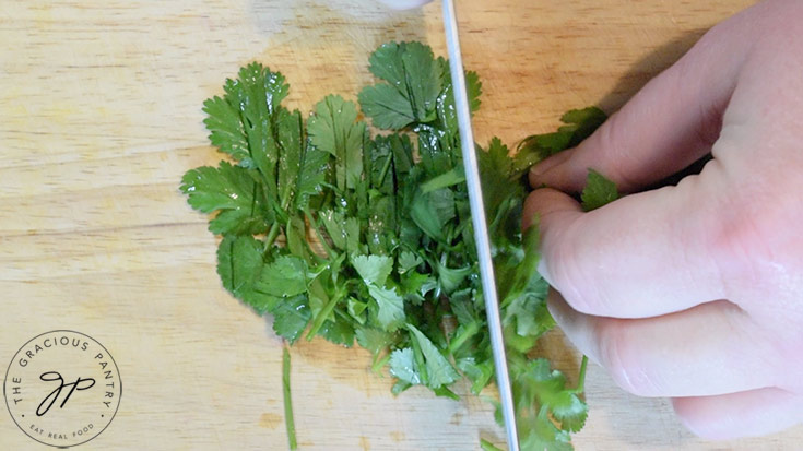 Fresh cilantro being chopped on a wooden cutting board.