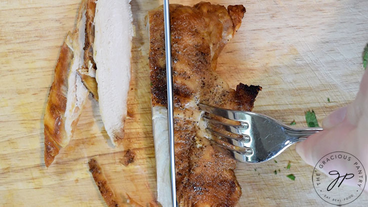 A cooked chicken breast being sliced on a wooden cutting board.