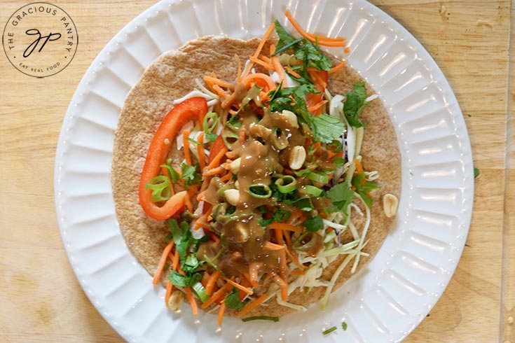 A tortilla with fresh veggies and chicken, with peanut dressing poured over the top.