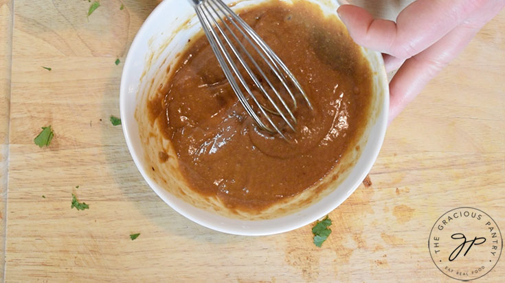 Peanut dressing being whisked together in a white mixing bowl for making Thai peanut chicken wraps.