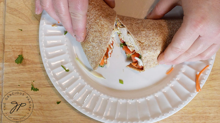 A Thai Peanut Chicken Wrap, sliced in half on a white plate.