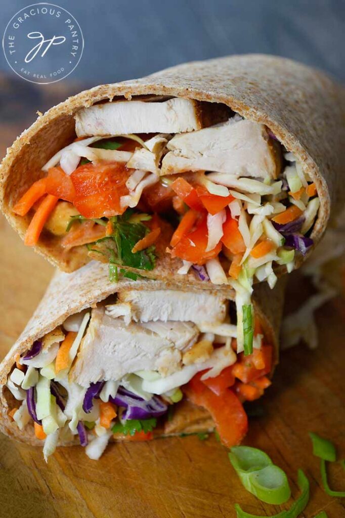 A front view of a slice Thai peanut chicken wrap sitting stacked on a cutting board.