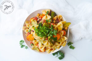 The finished Bow Tie Pasta Salad served in a white bowl and topped with fresh parsley.