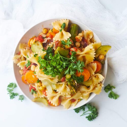 An overhead view looking down into a white bowl filled with Bow Tie Pasta Salad.