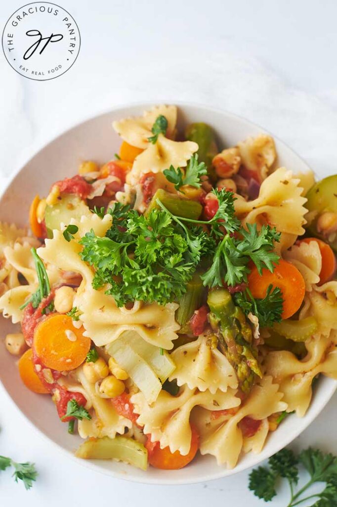 A close up overhead view of a white bowl filled with Bow Tie Pasta Salad.