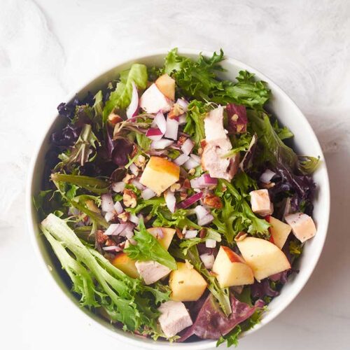 An overhead view of Chicken Apple Salad in a white bowl on a white background.