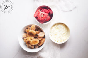 Three white bowls on a white surface. Once container frozen strawberries, the second frozen banana slices, and the third, cottage cheese.