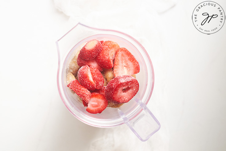 A blender tumbler holding all the ingredients for this Healthy Strawberry Ice Cream Recipe.